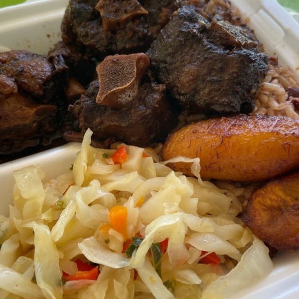 Island Vibes' oxtail with rice, fried plantains, and cabbage in a white takeout container.