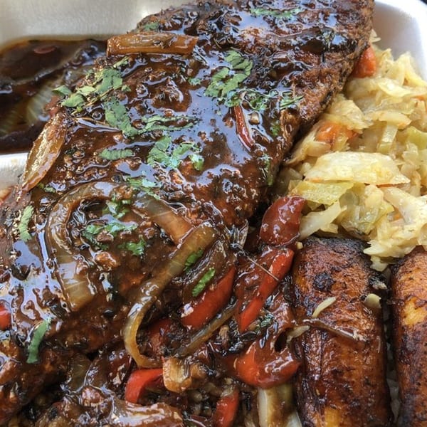 Island Vibes' brown stew fish with onions, peppers, cabbage, and plantains in a takeout container.