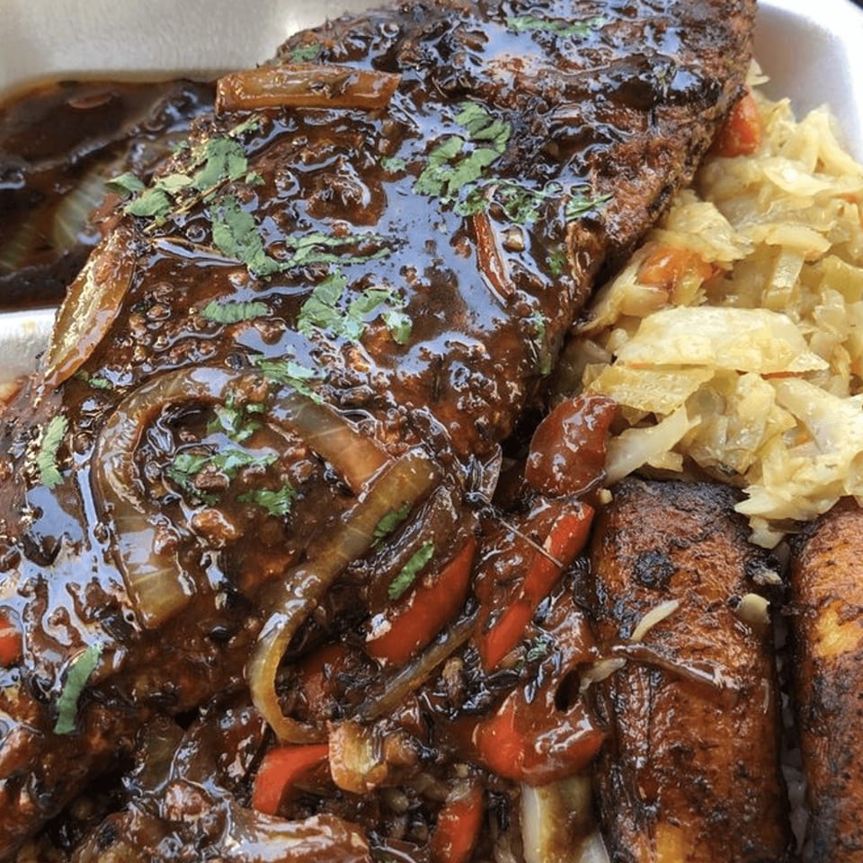 Caribbean brown stew fish with onions, peppers, and cilantro, served with cabbage and plantains.