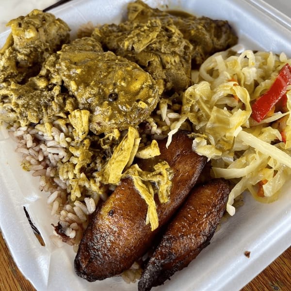 Curried chicken, rice and peas, fried plantains, and steamed cabbage in a white takeout container.