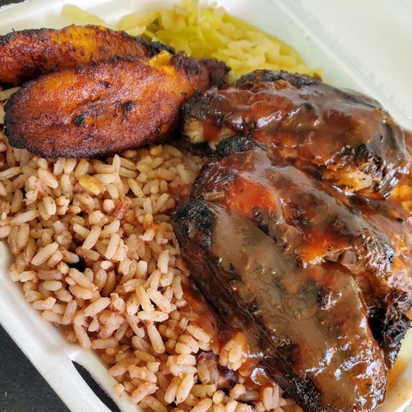Close-up of Island Vibes' jerk chicken with rice, plantains, and cabbage in a takeout container.